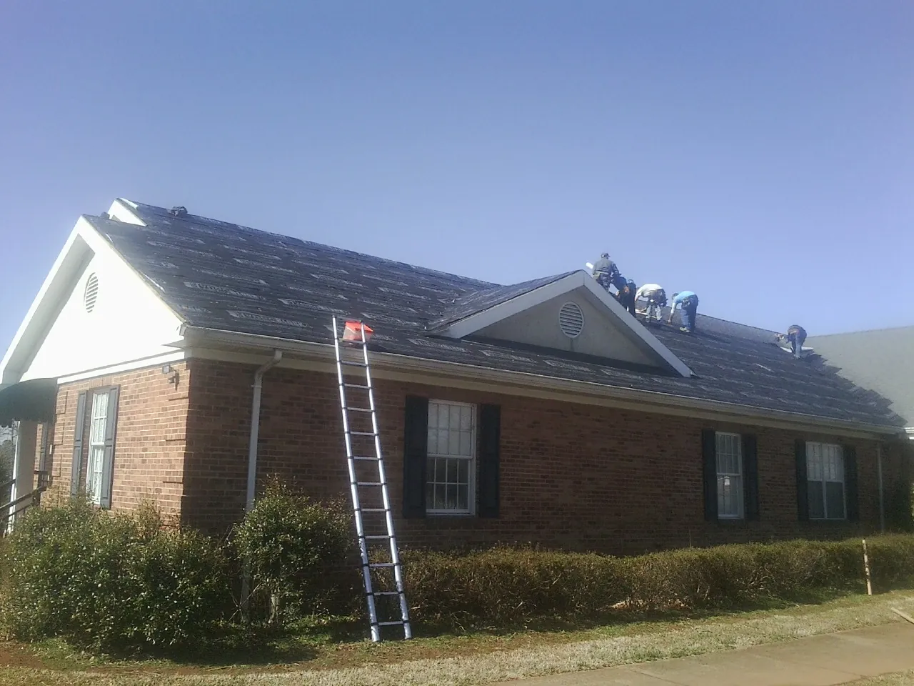 Crew tearing shingles off a brick ranch roof with a ladder set — Metal Roof Repair work by our crew in Murfreesboro