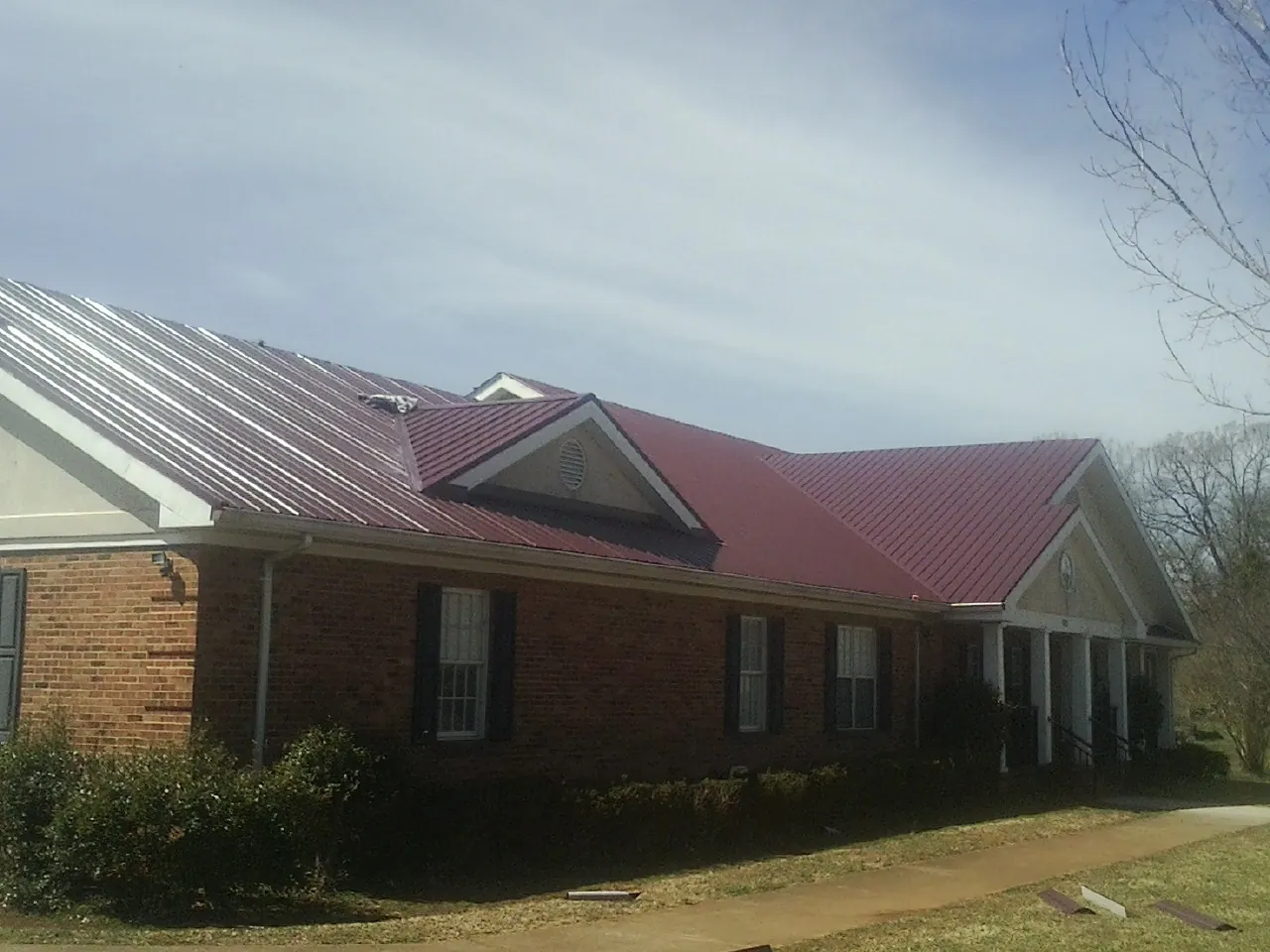 Red metal roof with gabled entries on a long brick building, from a Hail Damage Roof Repair job in Murfreesboro