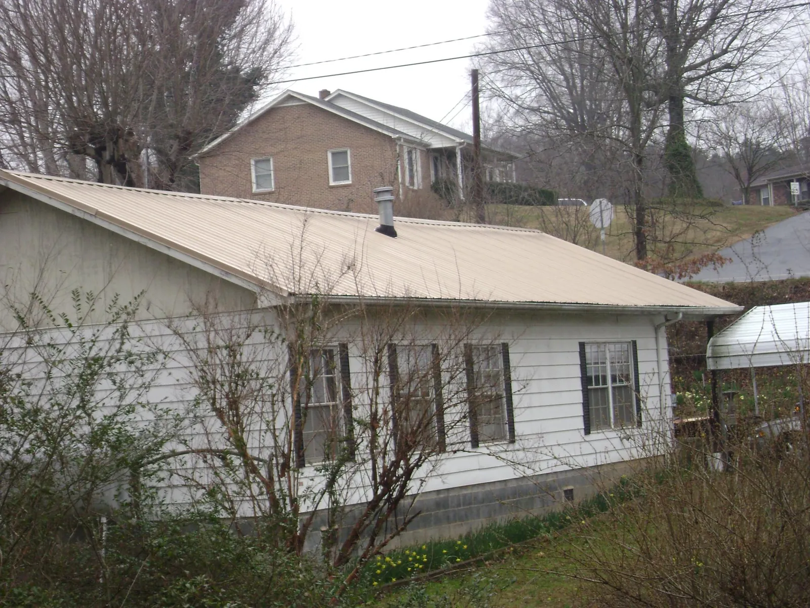 Tan metal roof on a white sided house set into a hillside — Commercial Roofing by Roofing Brothers in Murfreesboro